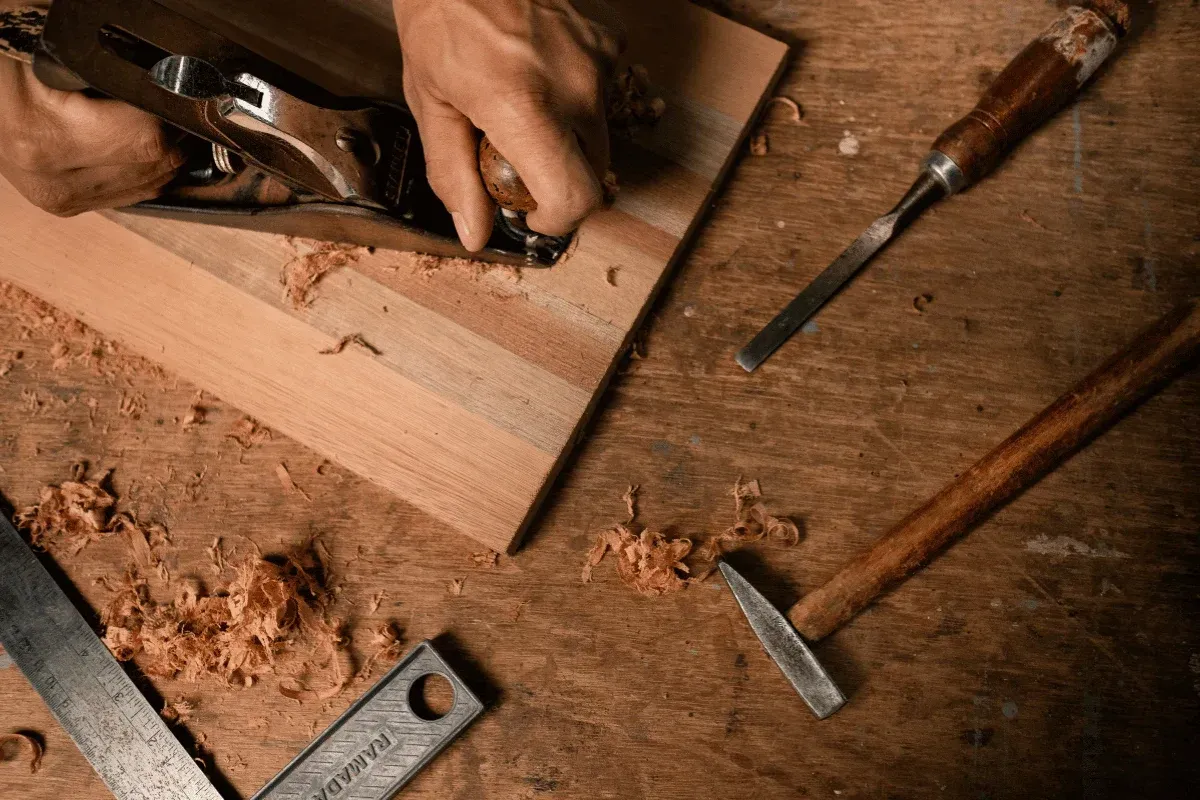 Mains d’un artisan rabotant une planche de bois dans son atelier