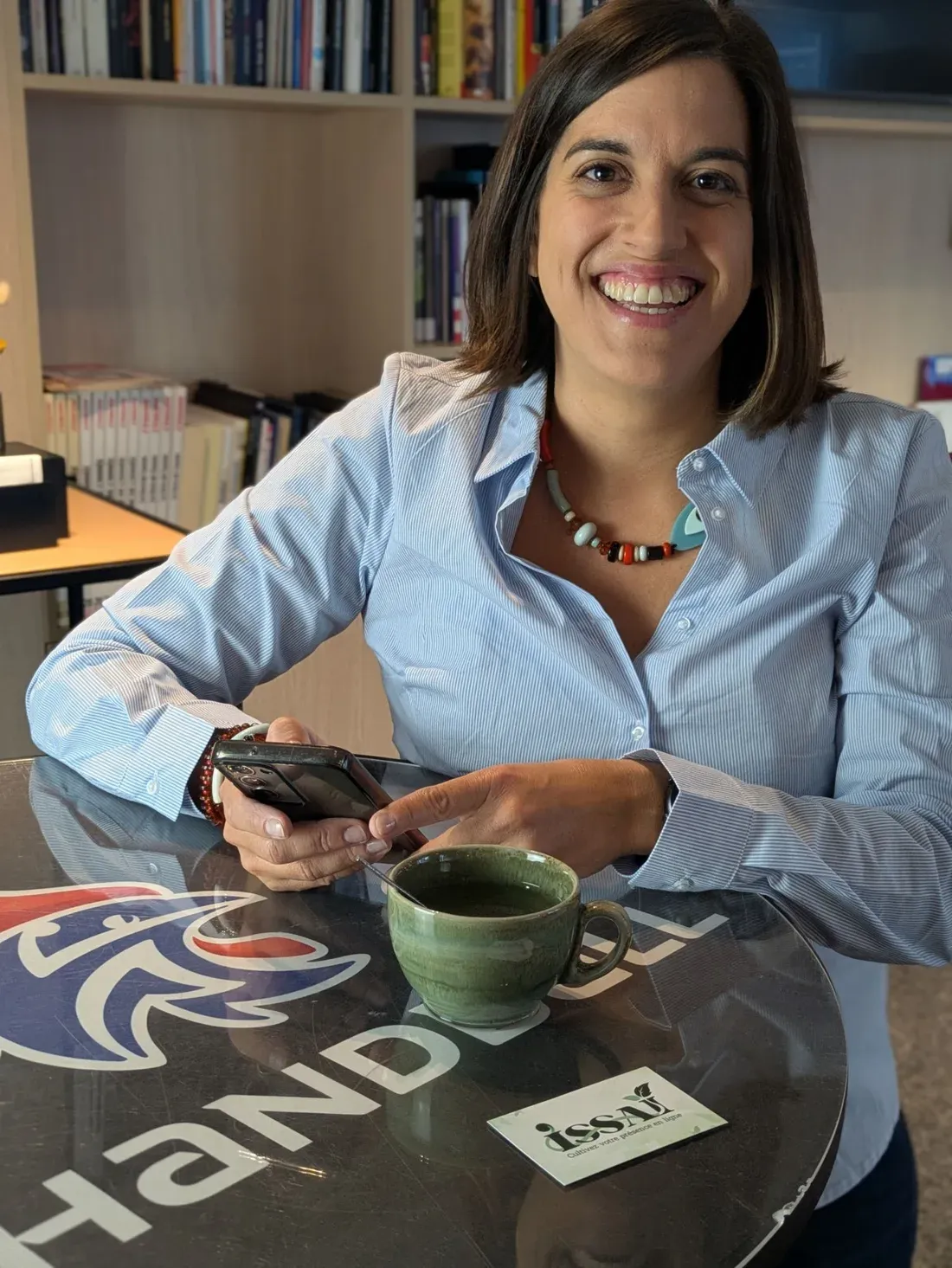 Bahia, fondatrice d’ISSAÏ, gère les réseaux sociaux sur son téléphone, carte ISSAÏ posée sur la table